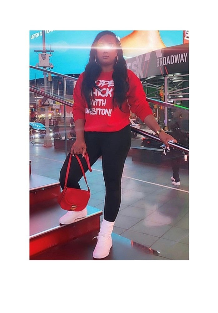 Podcast merch spotlight: Black woman in bold red ‘Dope Chick With Ambition’ sweatshirt stands on Times Square steps, urban empowerment, legacy branding, and unapologetic ambition.